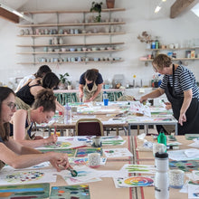 Load image into Gallery viewer, Art class in progress with students painting at tables in a studio setting.